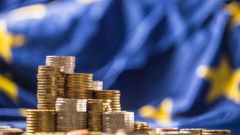 Geldmünzenstapel vor Europaflagge
